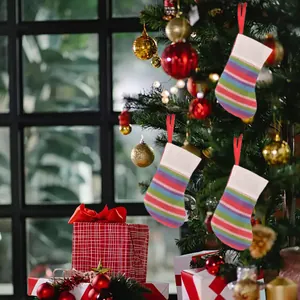 Mini colorful striped knitted Christmas stockings hanging on a festive decorated tree.