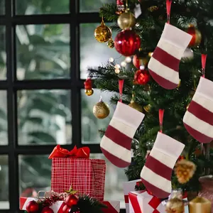 Set of 4 mini knitted striped Christmas stockings hanging on a festive decorated tree.