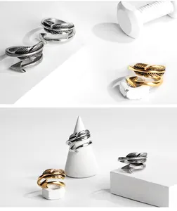 Detailansicht von Feder- und Pfeilringen in Silber und Gold auf minimalistischen Requisiten.