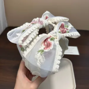 Detailaufnahme des weißen Spitzenstirnbands mit eleganten Blumenstickereien und Schleifen