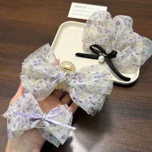 Detailansicht von eleganten Haarspangen und Haargummis mit lila Blumendruck aus Organza