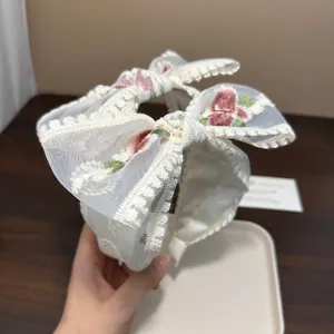 Detailaufnahme eines eleganten weißen Spitzenstirnbands mit zarter Blumenstickerei