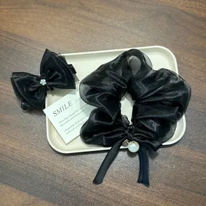 Macro detail showing a black organza bow hair scrunchie and clip set with pearl pendant.