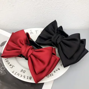 Vue détaillée de grandes pinces à cheveux à nœud en satin rouge et noir sur assiette blanche