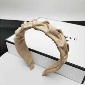 Detailaufnahme eines eleganten beigefarbenen Faltenstirnbands mit gedrehtem Design