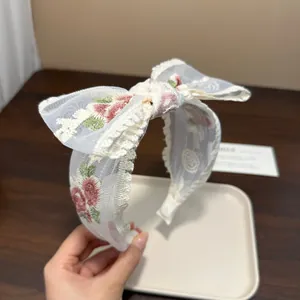 Detailansicht eines weißen Spitzenstirnbands mit Blumenstickerei und einer Schleife.