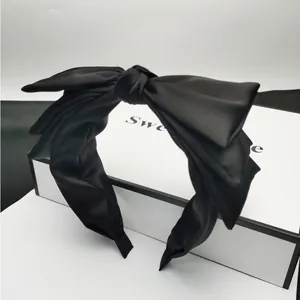 Dettaglio macro di un elegante cerchietto con fiocco in raso nero su una confezione regalo bianca