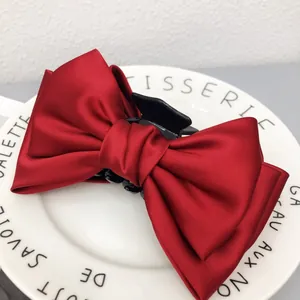 Gros plan d'une grande pince à cheveux avec nœud en satin rouge sur une assiette décorative blanche