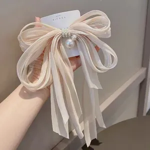 Primo piano di un fermaglio a fiocco color champagne con lunghi nastri e perle