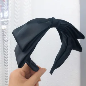 Close-up of black satin bow headband showing elegant texture and high skull top design.