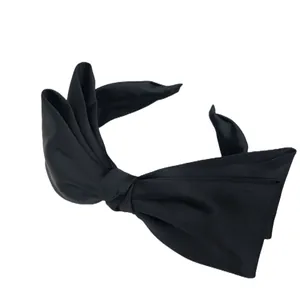 Close-up detail showing the fine fabric texture of the black satin bow headband.
