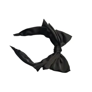 Dettaglio laterale di un cerchietto nero minimalista in raso con fiocco elegante