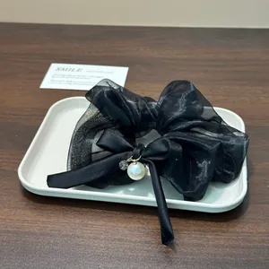 Close-up of a black organza scrunchie featuring a satin ribbon bow and a pearl.