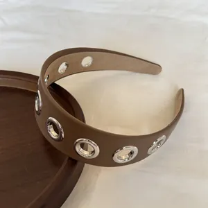 Dettaglio di una fascia punk in pelle marrone con occhielli in metallo argentato