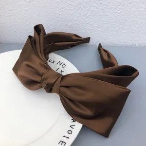 Close-up of a brown satin bow headband on a white decorative plate, highlighting silky texture.