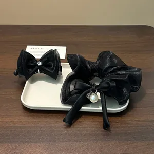 Elegant black mesh bow hair clip and pearl charm scrunchie set presented on white tray