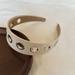 Dettaglio ravvicinato di un cerchietto in pelle crema con occhielli decorativi in stile punk