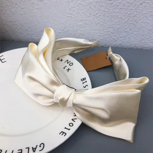 Detail view of a cream satin bow headband with elegant glossy texture and chic design