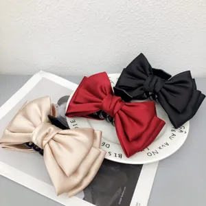 Vue détaillée de grandes pinces à cheveux en satin avec nœud en rouge, noir et champagne.
