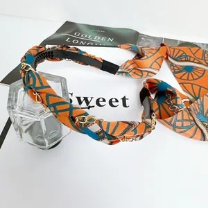 Dettaglio di una fascia retrò in raso con catena dorata e motivo arancione vintage