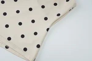 Detailopname van de fijne stiksels en het zwarte polkadotpatroon op de crème mouwloze top