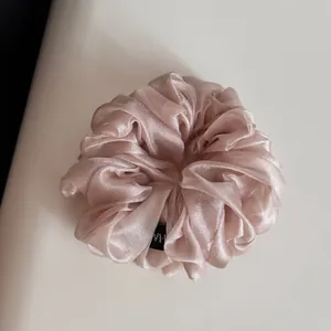 Gros plan d'un chouchou élégant en organza scintillant rose champagne à doux volants