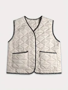 Detailed flat lay view of a chic quilted cream vest with black wavy trim and pockets.
