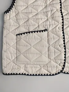 Detailed macro view of beige quilted vest featuring black crochet trim and buttons