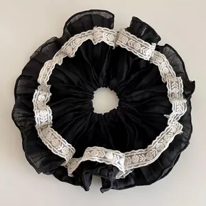 Dettaglio di un elastico per capelli nero plissettato stile francese con pizzo bianco.