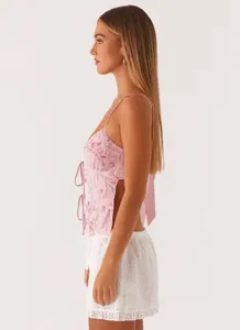 Side view of a pink sequined camisole top with lacing paired with white eyelet shorts.