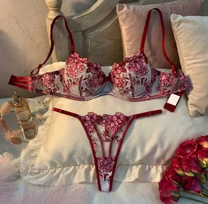 Detailed close-up of red floral embroidery on sheer mesh lingerie set on pillows.