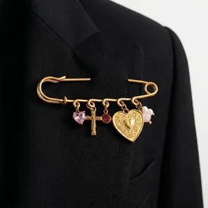Vue détaillée d'une broche épingle de sûreté dorée avec breloques cœur et croix de style vintage.