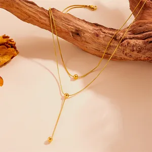 Vue détaillée d'un collier double épaisseur en acier inoxydable doré avec pompons