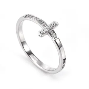 Detalle de un anillo de acero plateado con cruz de cristal y un grabado minimalista.