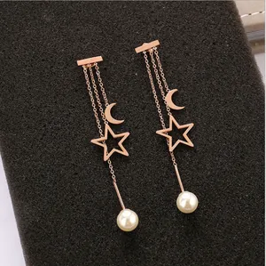 Detalle de pendientes largos de acero inoxidable rosa con dijes de estrella, luna y perla