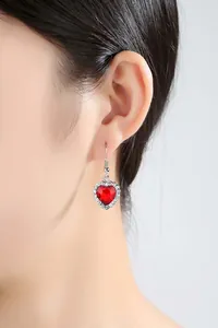 Nahaufnahme eines klassischen herzförmigen roten Kristallohrrings, am Ohr getragen