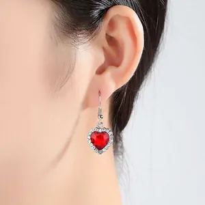 Elegante rote herzförmige Kristallohrringe mit weißen Steinen am Ohr eines Models