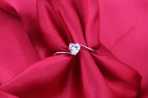 Detail shot of an elegant heart-shaped zirconia silver ring on a red silk background