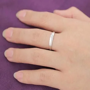 Detail view of a minimalist silver wedding ring with a sparkling zirconia on a finger.
