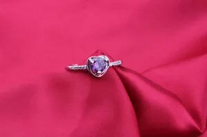 Macro detail of a silver ring with a vibrant purple heart-shaped zircon on red silk
