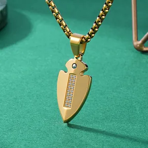 Gold titanium steel arrowhead pendant necklace with inset stones on green background.