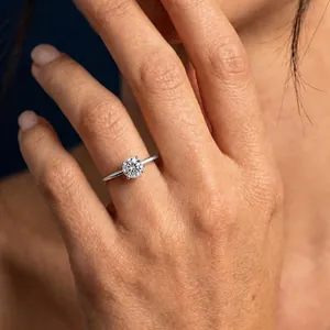 Close-up of a Moissanite solitaire ring on a finger, showing 4-prong silver setting.