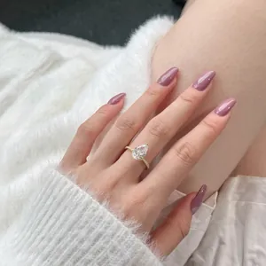 Gros plan d'une bague élégante taille poire portée sur une main soignée avec vernis mauve