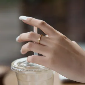 Gros plan d'une bague perlée dorée avec pierre carrée portée sur la main