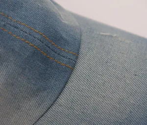 Nahaufnahme der gelben Doppelnähte und der Textur der hellblauen Jeans-Baseballkappe.