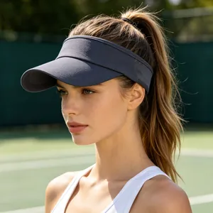 Side view of a woman wearing a dark grey athletic sun visor hat on a tennis court
