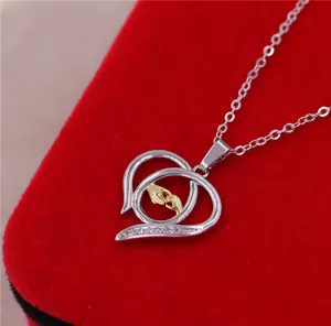 Primer plano de colgante corazón de plata con motivo dorado de mano grande sosteniendo pequeña