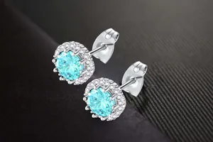 Close-up view of silver halo stud earrings with brilliant cyan zircon center stone