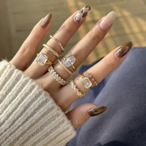Close-up of layered gold rings with emerald and oval cut stones on manicured hand.