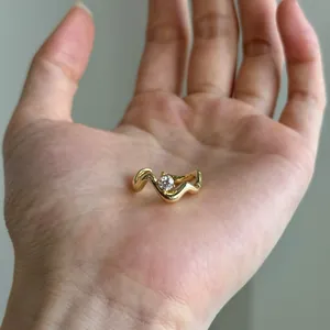 Detail view of a minimalist irregular wavy gold ring with a clear gemstone in palm